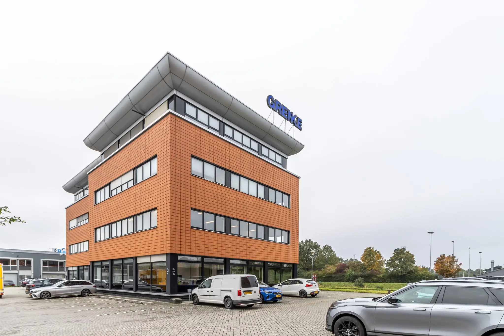 Modern kantoorgebouw aan de Lage Biezenweg met het logo van GRENKE op het dak en geparkeerde auto's op de voorgrond.